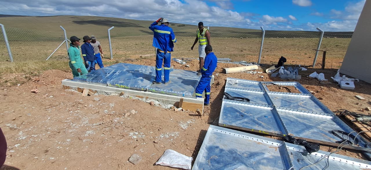 Installation team laying the base panels of the eZambuzane tank on a concrete plinth near Dutywa