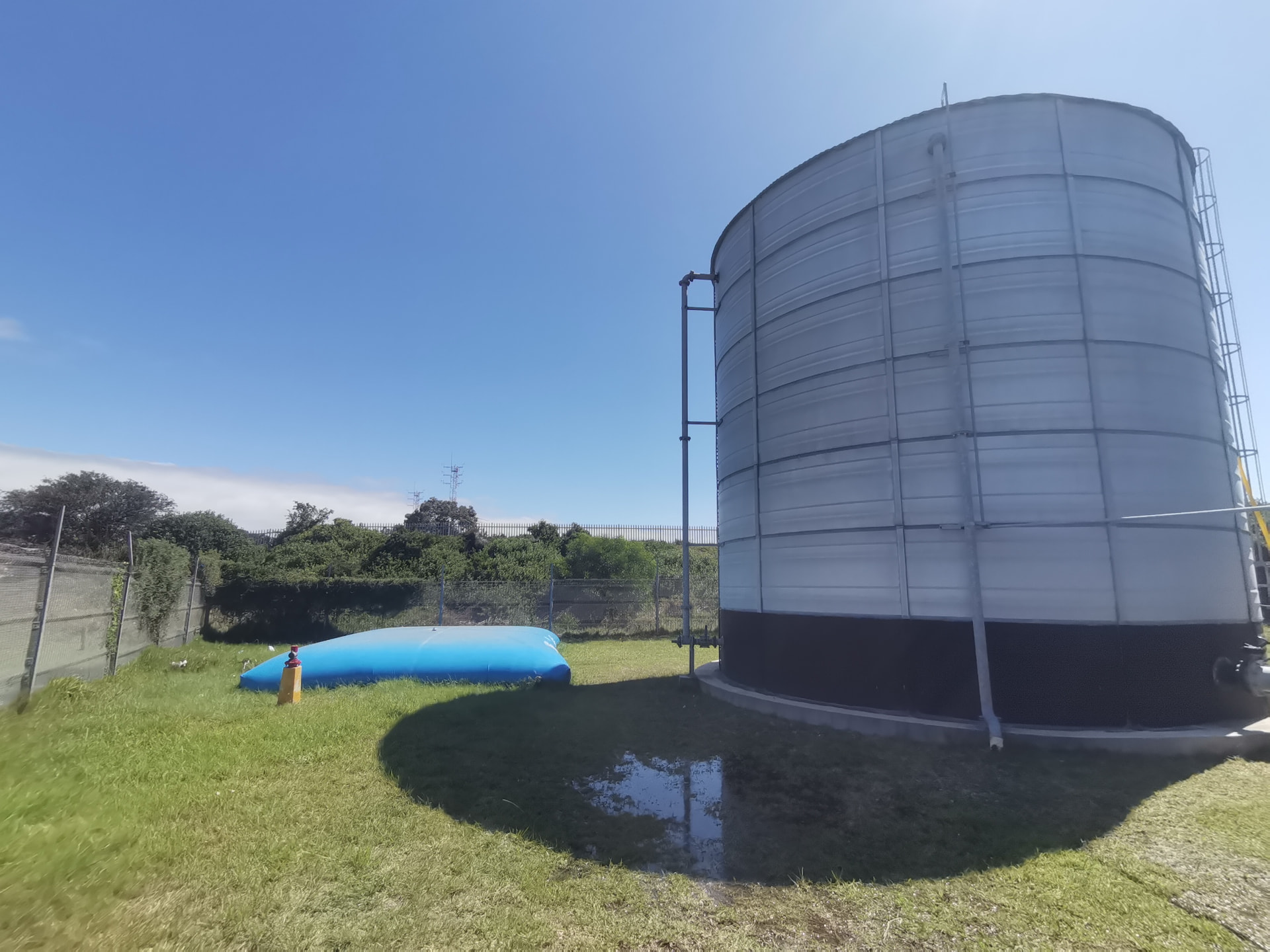 Temporary water storage bladder beside a commercial steel water tank