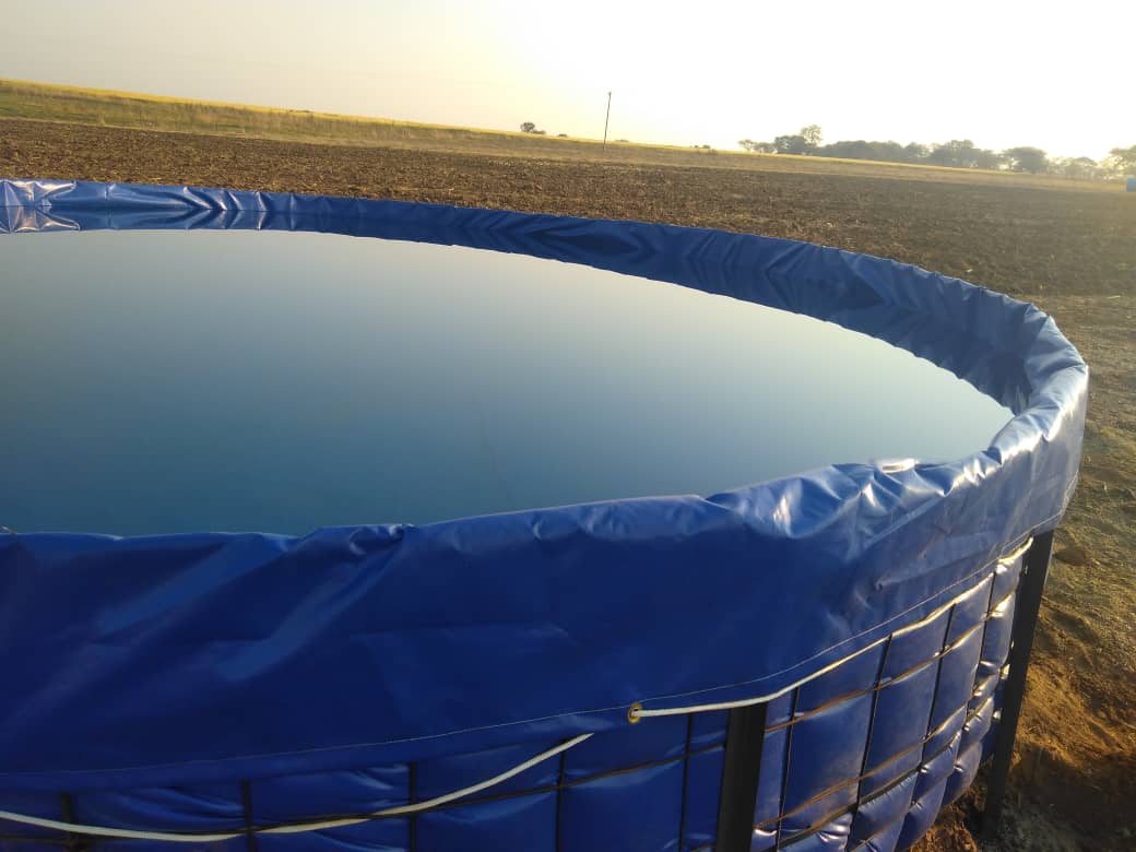 Circular PVC-lined water storage tank in open field